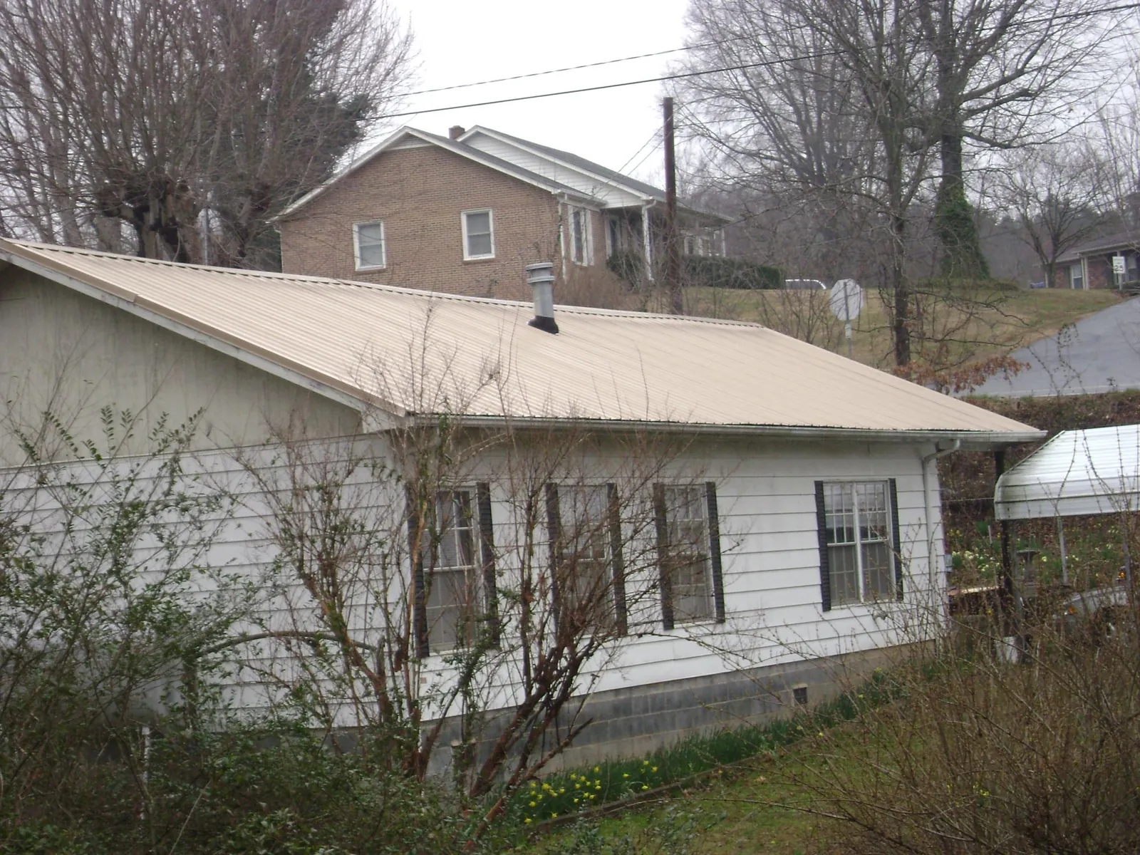 Tan metal roof on a white sided house set into a hillside — Commercial Roofing by Roofing Brothers in Weston